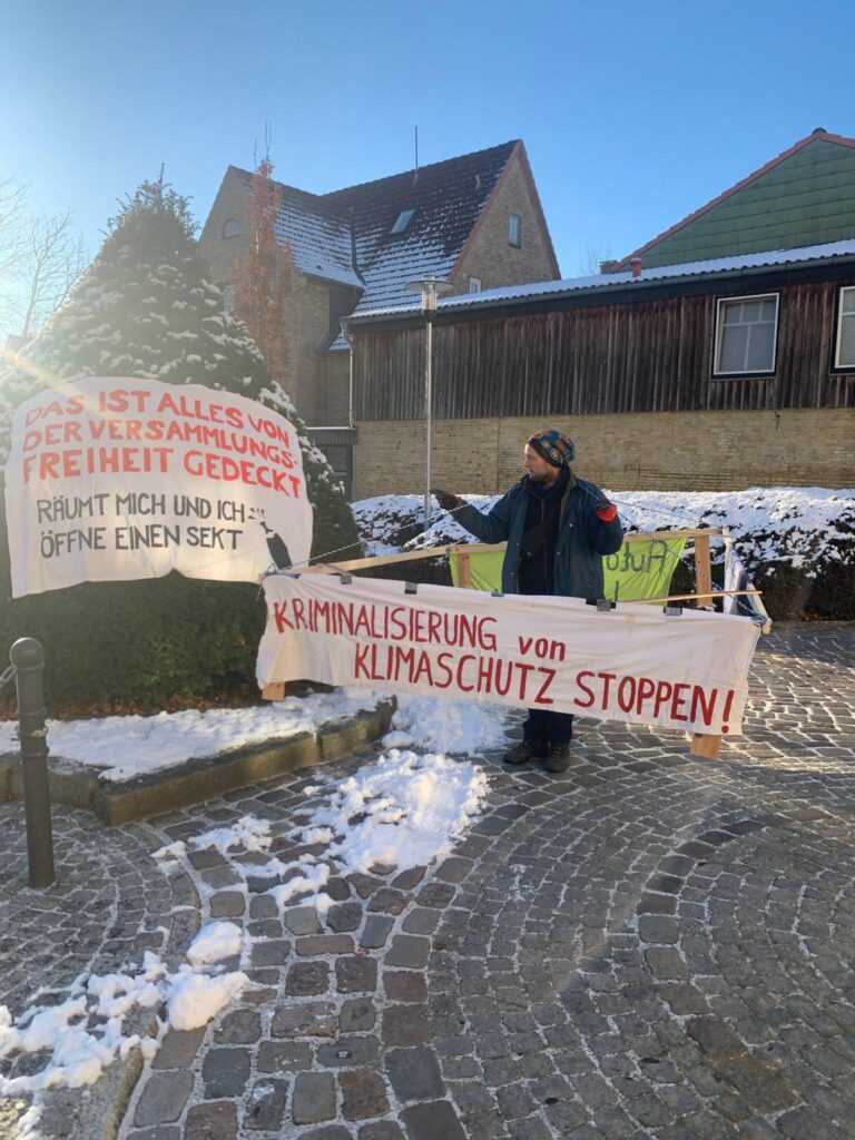 Mensch mit Gehzeug mit Schild "Kriminalisierung von Klimaschutz stoppen"