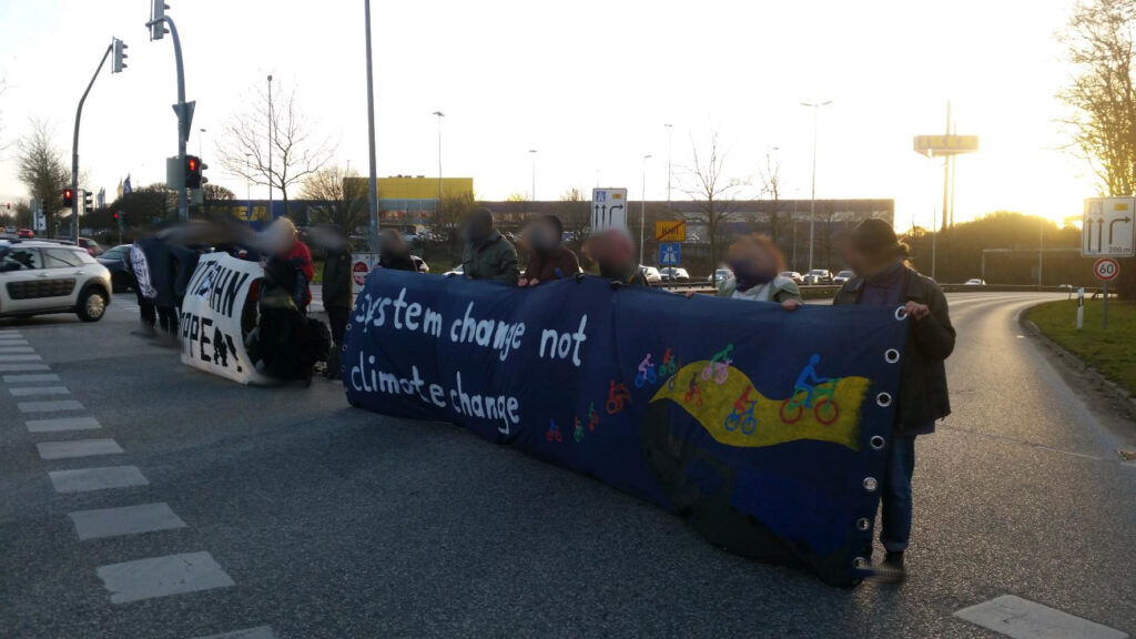 Menschen stehen auf der Straße und halten ein Transparent "System change not climate change"
