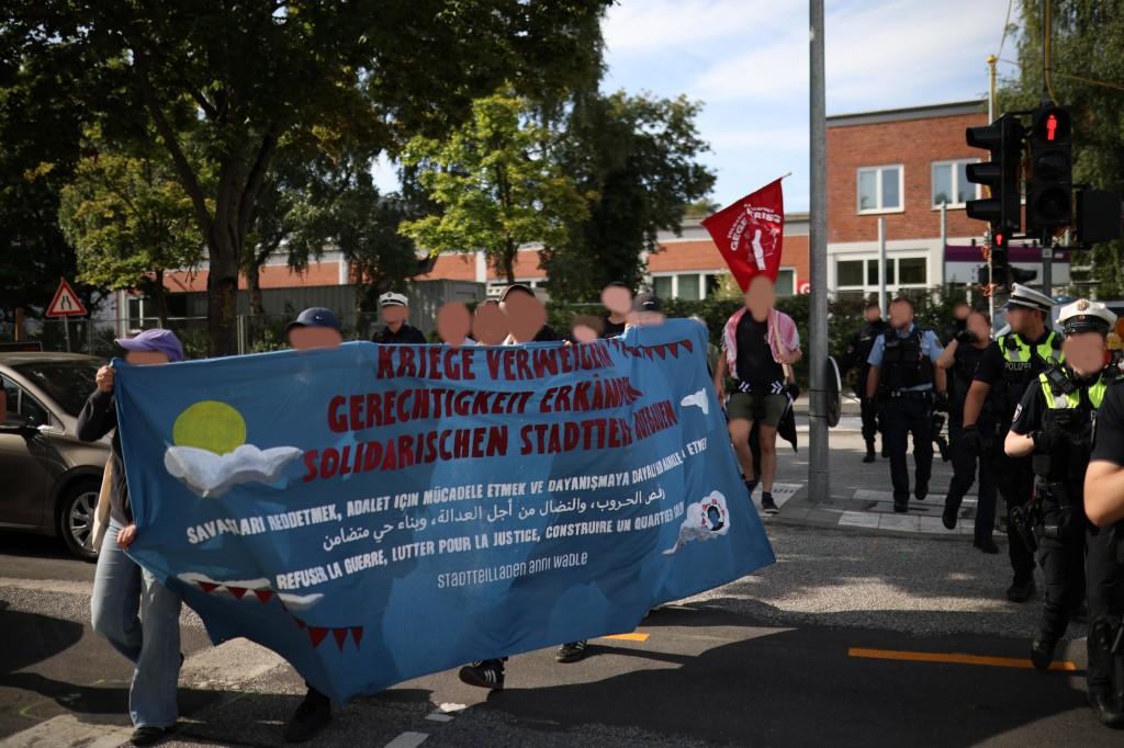 Menschen kommen über eine Straße mit einem blauen Transparent mit viel Text, begleitet von Cops.